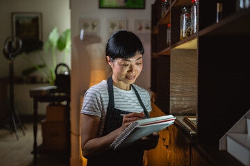 japanese woman artisan write recipes at notebook in herbal workshop