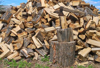 A large pile of firewood with an axe stuck in the log. The image shows hard physical labor and a rural lifestyle. Suitable for projects related to nature, work, or winter.