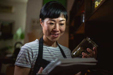 japanese woman artisan read recipes at notebook in herbal workshop