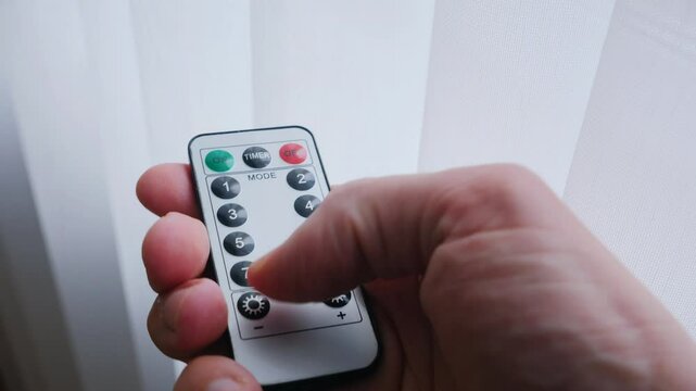 A hand holds a small, white remote, ready to adjust the lighting. Adjusting the mood with a simple touch, the remote in hand. 