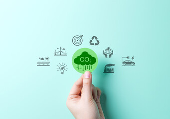 Reducing CO2 Emissions and Promoting Sustainability Concept. A hand holds green CO2 cloud icon with environmental symbols, such as solar, wind turbines, and recycling. Reduce carbon and go green.