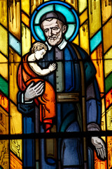Fototapeta premium Stained glass of St. Vincent de Paul carrying a child in his arms.