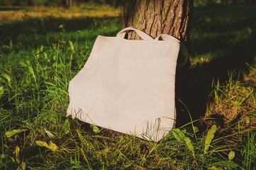 White canvas tote bag mockup template with long handles among the green plant leaves near the tree...