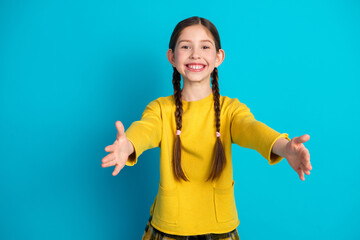 Happy young girl in a yellow sweatshirt smiling and reaching out against a vibrant blue background in a cheerful and inviting pose
