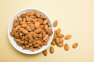 Top view of almonds into bowl on yellow background.