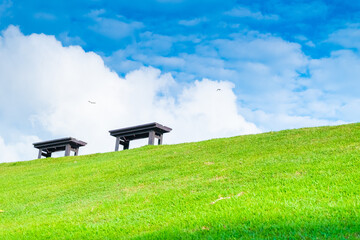 Garden bench with Green meadows with blue sky and clouds background, Landscape view of green grass on slope Scenic panoramic view on a beautiful sunny day,japanese picture concept.
