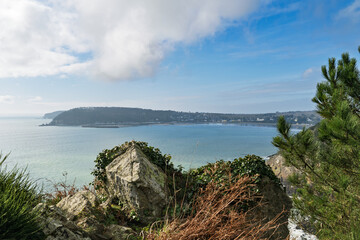 La baie de Morgat, vue depuis les falaises, s’illumine sous un ciel bleu parsemé de nuages blancs.