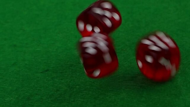 Three red casino dice falling on a green felt in slow motion, close-up