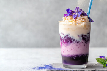 Delicious layered purple smoothie topped with whipped cream and edible flowers served in a glass with a straw.