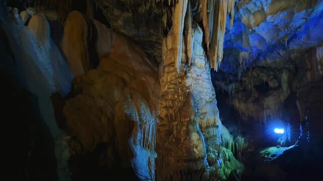 The bright and colorful Abrskil cave. A gallery-type cave in the mountains of Abkhazia with many stalactites and stalagmites, colorful lighting. Otapskaya (Otap cave). 4K