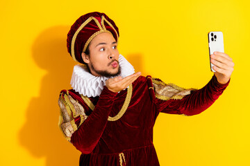 Young man dressed as a historical nobleman takes a selfie with a modern smartphone against a...