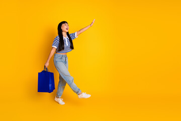 Young woman stands against a yellow background holding a shopping bag while joyfully gesturing
