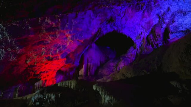 The bright and colorful Abrskil cave. A gallery-type cave in the mountains of Abkhazia with many stalactites and stalagmites, colorful lighting. Otapskaya (Otap cave). 4K