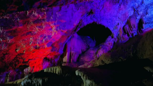The bright and colorful Abrskil cave. A gallery-type cave in the mountains of Abkhazia with many stalactites and stalagmites, colorful lighting. Otapskaya (Otap cave). 4K	