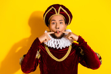 Modern young man dressed as a medieval nobleman making a fun facial expression in costume on a bold yellow background.