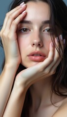 Fototapeta premium This stunning portrait captures a young woman with expressive eyes and flawless skin, framed by her gently placed hands. The image radiates a sense of vulnerability and beauty, inviting viewers to