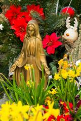 Statue of Virgin Mary blessing surround by flowers.