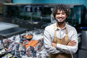 A smiling fishmonger stands confidently in front of a display of fresh seafood, ready to assist customers. He wears an apron.