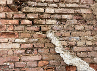 Close-up of an old red brick wall with cracks, erosion, and remnants of white plaster. A textured...