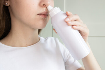 Close up of woman performing nasal rinse with saline spray bottle to maintain nasal hygiene and...