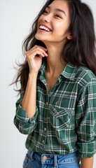 Fototapeta premium A cheerful young woman with long, flowing hair radiates happiness while wearing a stylish green plaid shirt. Her warm smile and playful pose create an inviting atmosphere, perfect for showcasing