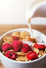 Pouring milk into bowl of cereal with raspberries and strawberries for breakfast