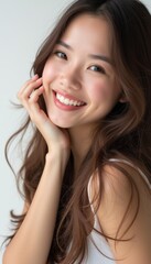 A cheerful young woman with long, wavy hair beams with joy, her hand gently resting on her cheek. Her glowing complexion and infectious smile radiate warmth and positivity, inviting viewers to share