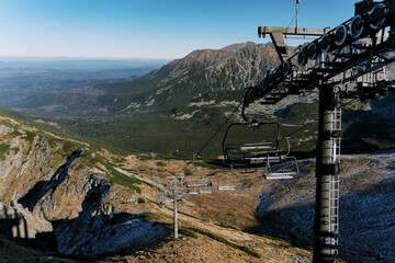 A breathtaking view from a high-altitude chairlift, overlooking rugged peaks and lush valleys. The ski lift structure contrasts with untouched nature, creating a striking adventure scene.