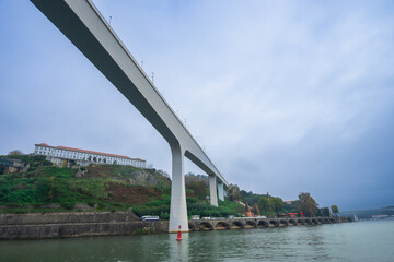 Obraz premium View of Arrabida Bridge, a modern concrete arch bridge in Porto, from a Douro River cruise on a cloudy afternoon.