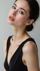 Fototapeta premium This striking portrait captures a young woman with delicate features, exuding confidence and poise against a minimalist background. Her subtle makeup enhances her natural beauty, while the soft