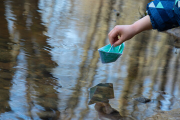 a child launches a paper boat in a puddle in spring