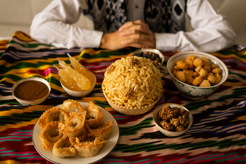 Colorful Uzbek table setting with traditional sweets. A large bowl of chak-chak, adorned with...