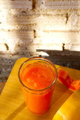 Papaya juice with blurred papaya slice on brick wall. Papaya glass smoothie with morning light. Freshness, summer, healthy drink, beverage, water, vegan, good food, fresh juice, natural light concept.