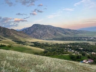 Fototapeta premium rolling green hills and rugged mountains at sunset with a rural village and river in a picturesque valley, ideal for travel
