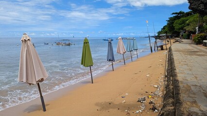 Ocean at high tide with a row of sun parasol umbrellas on sandy beach in water in Sanur, Bali, Indonesia 