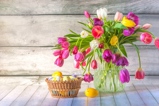 Happy easter holiday concept; bunch of multicolored tulps in vase and easter eggs in a basket on a wooden background