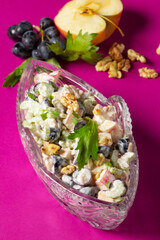 Waldorf salad with apples, celery, grapes and walnuts, dressed with mayonnaise and sprinkled with parsley in a crystal salad bowl.