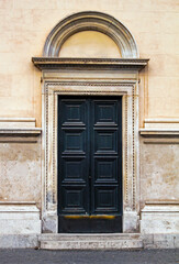 Fototapeta premium Old closed wooden black door on urban building stone facade in street