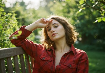 Woman in red shirt rests on bench with hand on forehead outdoors light