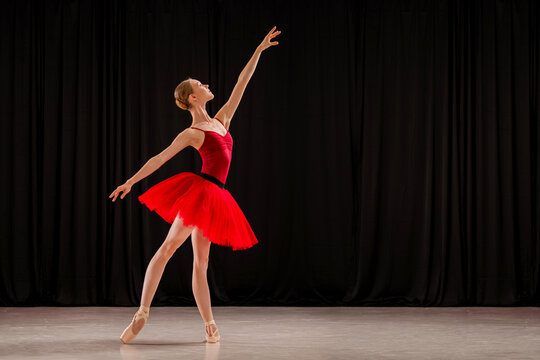 ballerina in a vibrant red dress performs a variation on stage. Capturing the grace and skill of ballet in a dynamic pose.