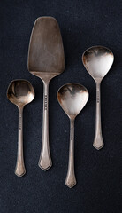 Elegant Silver Serving Utensils Set. Different spoons cutlery on a black background. Dessert cake...