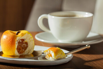 Mousse cake with peach filling covered with velvet glaze and a cup of latte on a table in a cafe.