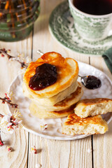 Lenten yeast pancakes with plum jam and tea, and a bouquet of flowering apricot branches on a light wooden table.