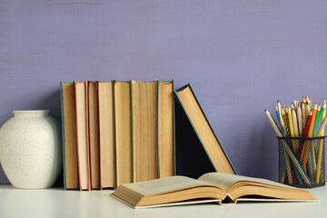 Open book lies on white table near stack of old books and colored pencils