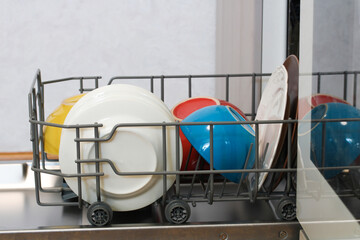 Open dishwasher with colorful clean dishes inside, ready for unloading