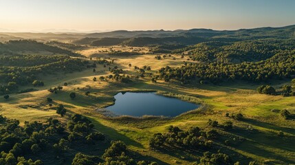 Naklejka premium Serene Aerial View of Lush Green Valley with Scenic Lake and Rolling Hills