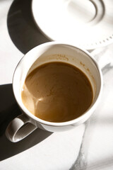 Hot coffee white cup and coasters placed on grey table with morning sunlight. Close-up coffee cup latte in vertical. Milk coffee, shadow, coffee texture, energy drink, cafe, and relaxation concepts.