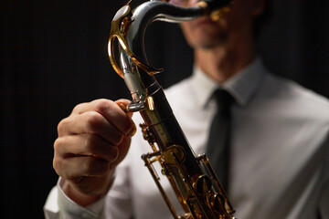 Close up on hand of male musician tightening neck screw on shiny tenor saxophone tuning up...