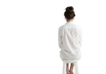 A woman sitting on a white stool with her back to the viewer wearing a white button down shirt on transparent background