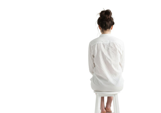 A woman sitting on a white stool with her back to the viewer wearing a white button down shirt on transparent background